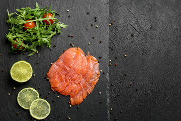 Fresh sliced salmon fillet with arugula and lemon on slate plate, top view