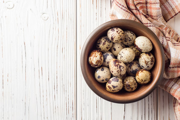Fresh quail eggs in ceramic bowl on white wooden background