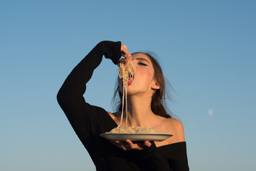 Young beautiful woman eating spaghetti, on blue sky background