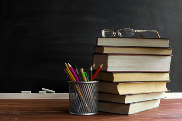 Glasses teacher books and a stand with pencils on the table, on the background of a blackboard with chalk. The concept of the teacher's day. Copy space.