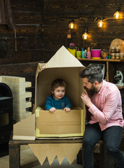 Parenthood concept. Boy play with dad, father, little cosmonaut sit in rocket made out of cardboard box. Kid happy sit in cardboard hand made rocket. Child boy play cosmonaut, astronaut.