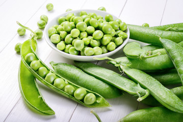 Shelled and unshelled peas on white wood background