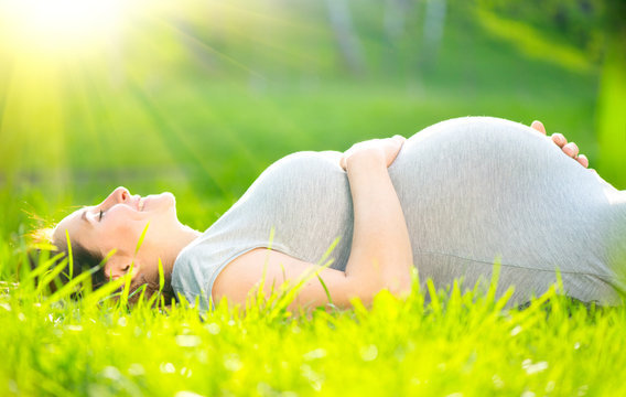 Pregnant middle aged woman touching her belly lying on green grass, enjoying nature, Healthy Pregnancy concept