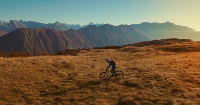 Aerial tracking shot of mountain cyclist cross-country riding with amazing mountain peaks in background.