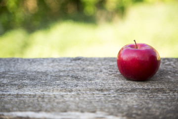 Apple on a wooden table against of blurry leaves