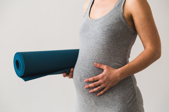 Young woman in early pregnancy with rolled mat under her arm going to prenatal yoga class