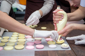 cooking, food and baking concept - chef with confectionery bag squeezing cream filling to macarons shells at pastry shop