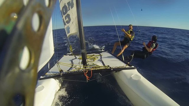 Fastened by ropes catamaran windsurfers overhanging hull, waving at passing bird