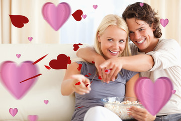 Cute couple watching TV while eating popcorn against love heart pattern