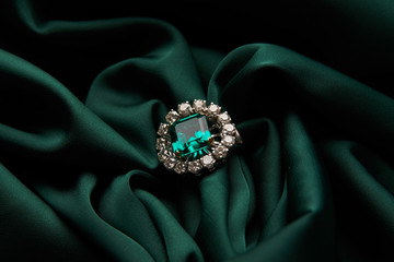 Green emerald fashion engagement diamond ring on green satin background. Luxury female jewellery, close-up. Selective focus - obrazy, fototapety, plakaty