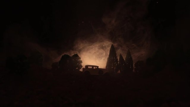 Silhouette of old vintage car in dark foggy toned background with glowing lights in low light, or silhouette of old car in dark forest. Selective focus