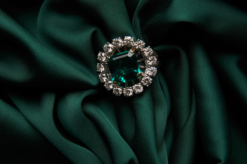 Green emerald fashion engagement diamond ring on green satin background. Luxury female jewellery,...