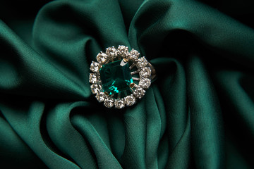 Green emerald fashion engagement diamond ring on green satin background. Luxury female jewellery,...