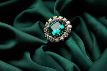 Green emerald fashion engagement diamond ring on green satin background. Luxury female jewellery,...