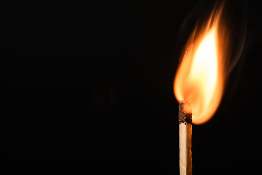 Match with strongly flaring flame on a black background closeup