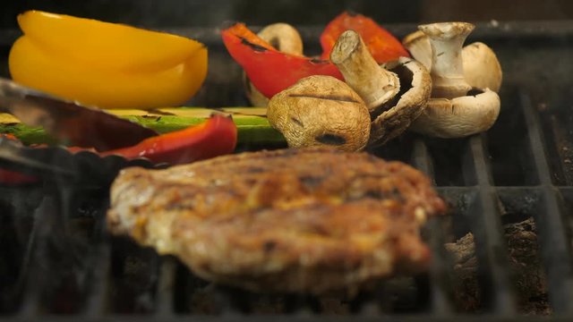 Large juicy marinated steak piece is focused, in the background grilled vegetables, zucchini, colorful peppers, tomatoes, mushrooms, focus on vegetables, macrobiotic
