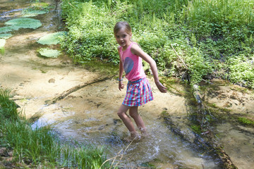 Child cute blond girl playing in the creek. Summer children fun.
