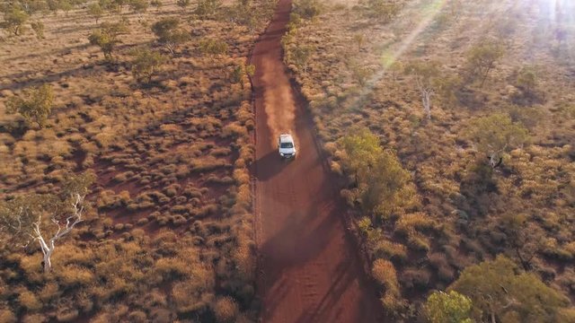 Aerial view of vehicle driving on dirt road through the Australia outback in the desert of Karijini NP with sun flares.