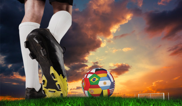 Composite image of football boot kicking flag ball against green grass under dark blue and orange sky