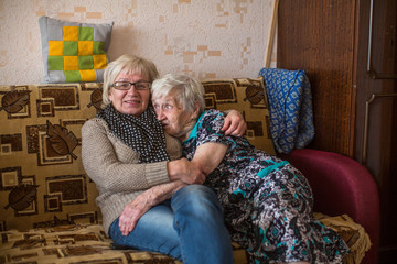 Elderly woman with her adult daughter in his house sitting on the couch.