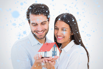 Attractive young couple holding a model house against snow falling