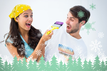 Happy young couple painting together and laughing against snowflakes and fir trees in green
