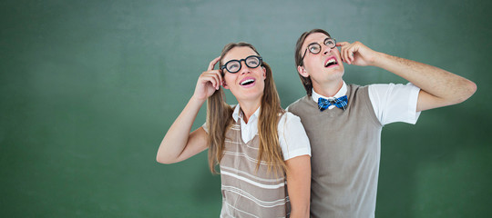 Geeky hipsters looking confused  against green chalkboard