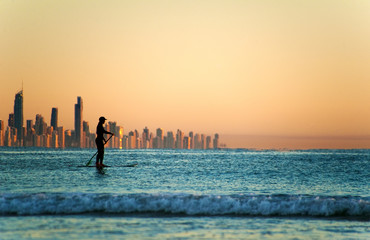 Single paddler against the Gold Coast skyline at sunset.
