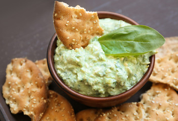 Bowl with tasty spinach sauce and crackers on wooden tray