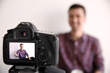 Male blogger on camera screen near light wall, closeup