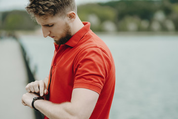 Young blonde man setting sportwatch before running in the morning.