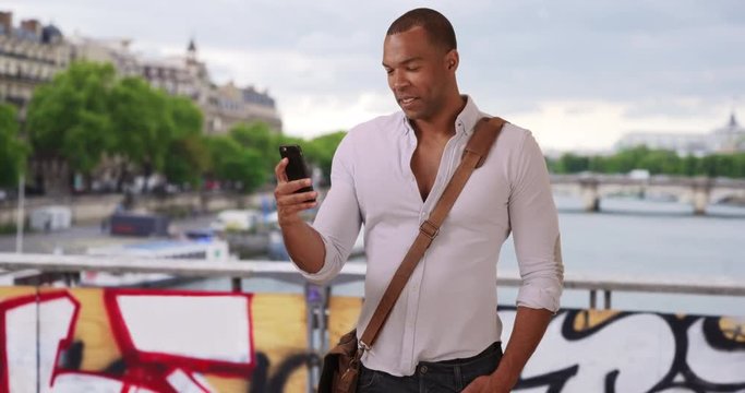 Attractive Black man traveling in Paris, France using his smartphone outside, Young male African-American tourist chatting with friends via text in Paris, 4k