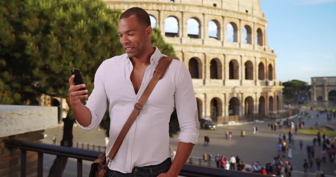 Vacationing young African-American male sending text messages to people back home while in Rome, Italy, Casual modern black man take photos of Rome on his phone near the Colosseum, 4k