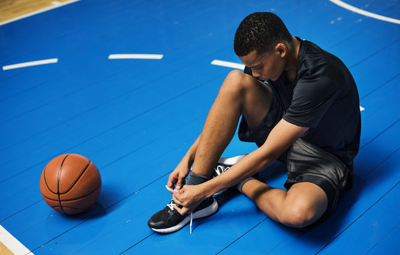 African American teenage boy tying his shoe laces on a basketball court