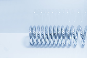 The  industrial coil spring  on the white background in the light blue scene.The  coil spring for industrial purpose.