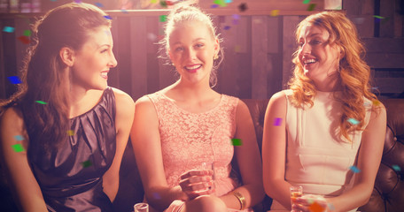 Three female friends holding shot glass of tequila in bar against flying colours