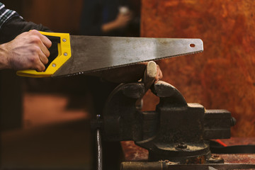 Man working in carpentry workshop. He cuts off excess part of saw from wooden handle of ax. Men at work. Hand work.