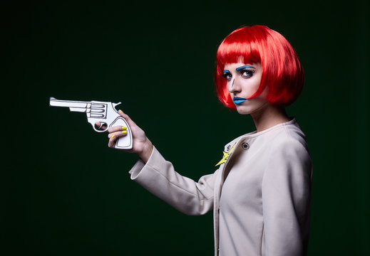 Portrait of young woman in comic pop art make-up style. Female with gun in hand