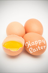 happy easter against three eggs with raw yolk in half a shell