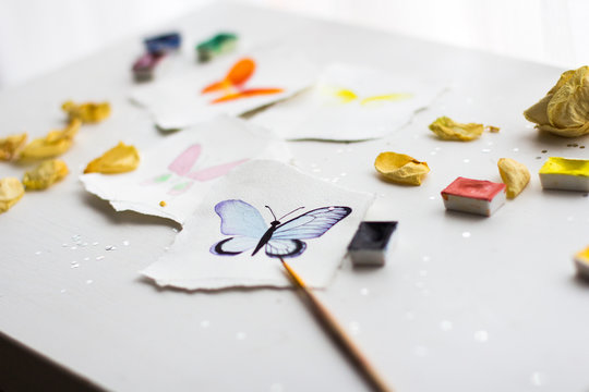 watercolor sketches of butterflies on the paper with torn edges on a white background with decorations, confetti, and dried flowers