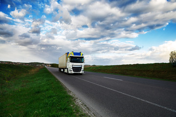 Fototapeta na wymiar Arriving white truck on the road in a rural landscape at sunset
