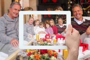 Hand holding tablet pc against multi generation family smiling at camera during christmas