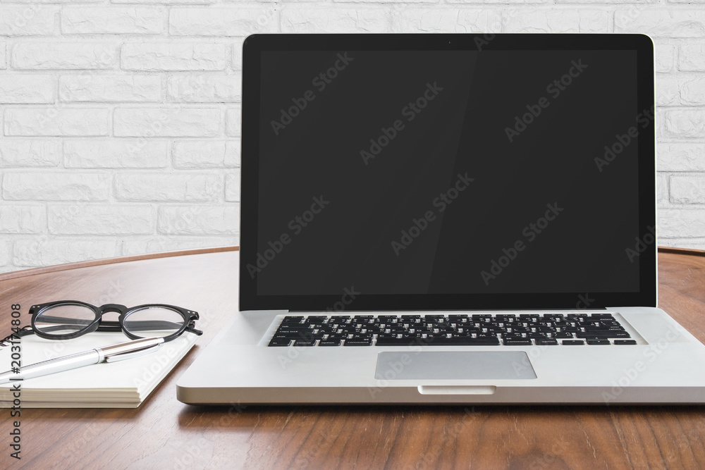 Poster notebook computer and note book paper on wooden table with white brick wall background.