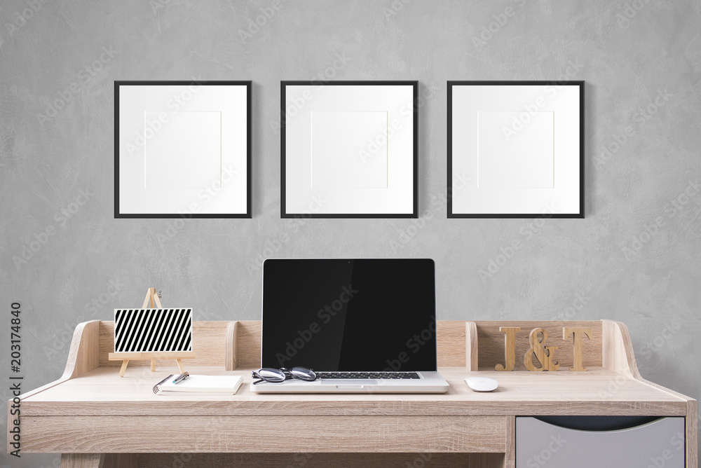 Fototapete notebook computer and stationery on working table with blank photo frames in the studio with cement 