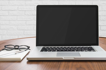 Notebook computer and note book paper on wooden table with white brick wall background.