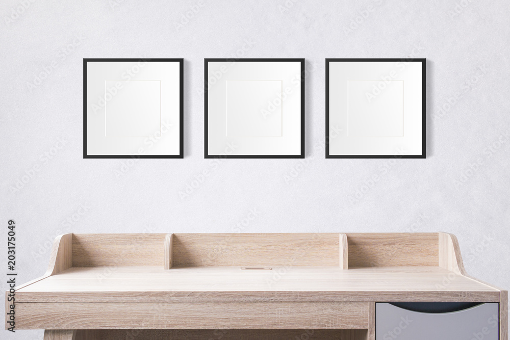Poster working table with blank photo frames in the empty studio with white concrete wall.