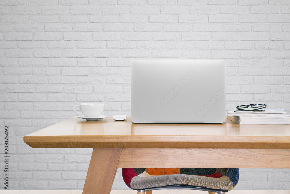 Poster notebook computer and a cup of coffee on working table in studio with white brick background
