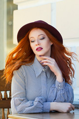Stylish young beautiful red-haired girl in a burgundy hat in a street cafe - 203176212