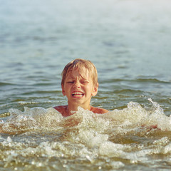 Happy little boy swimming in the river on summer weekend, image with square aspect ratio and warm...