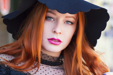 Portrait of stylish young beautiful red-haired girl in a black hat in a street cafe - 203176838